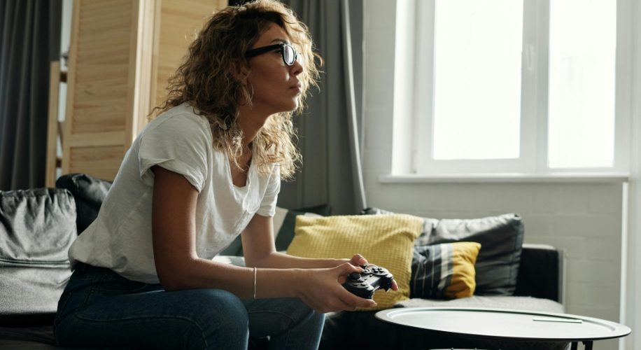 Woman with glasses intensely playing a video game with a controller.