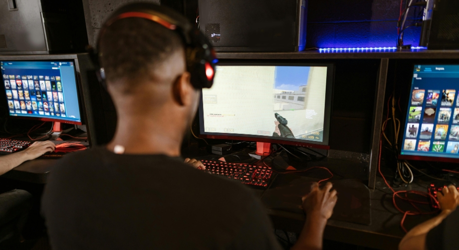 Person wearing headphones playing a first-person shooter game on a computer with RGB keyboard and mouse.