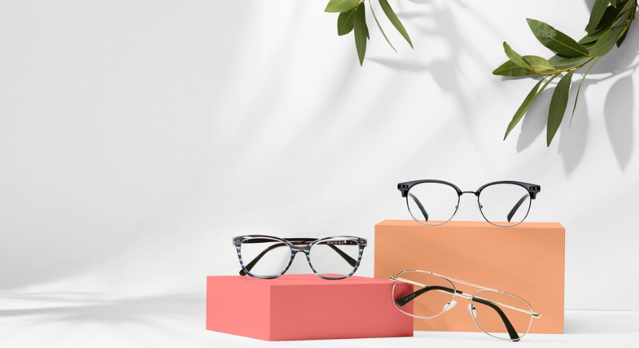 Three pairs of eyeglasses on red and orange pedestals, with greenery in the background.