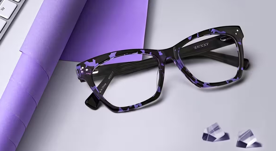 Purple and black ZENNI eyeglasses with rectangular frames and clear lenses, placed on a gray surface.