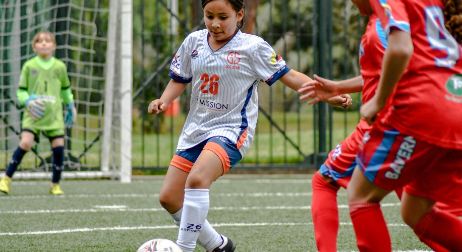 Young soccer player in a white jersey with number 26 dribbling the ball during a game.