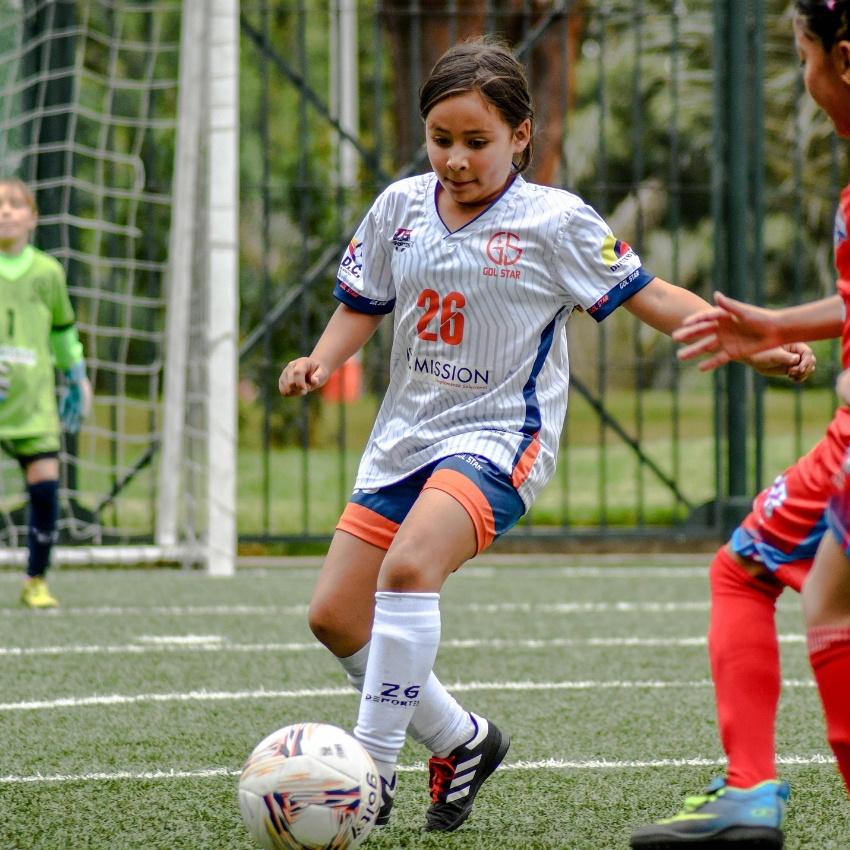 Youth soccer match, player in a white and blue jersey with number 26, "GOLSTAR MISSION" on front, controlling the ball.