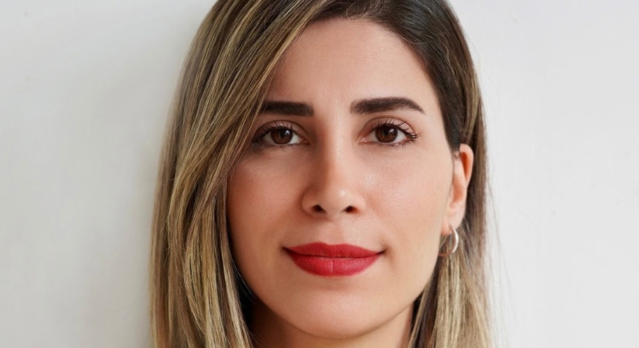 Woman with straight, shoulder-length blond hair and red lipstick, facing the camera against a plain background.