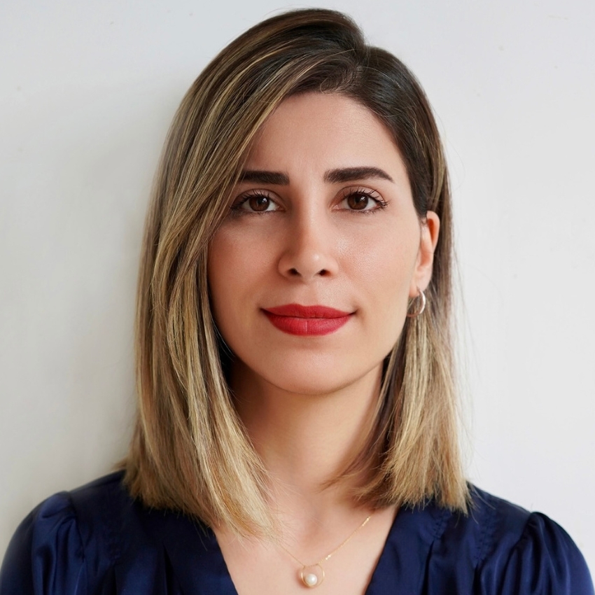 Woman with shoulder-length hair, wearing a dark blue top, red lipstick, and a pearl necklace.