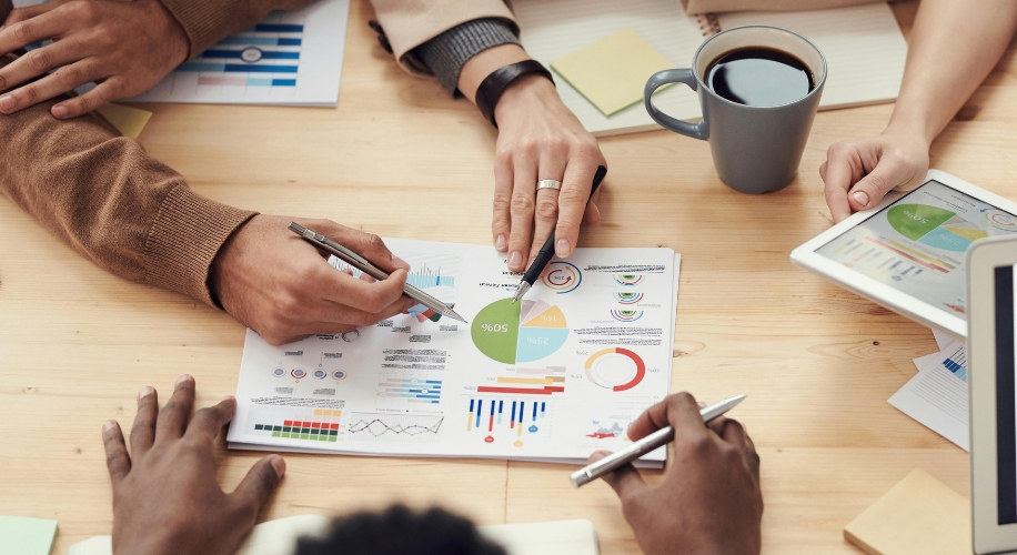 Hands pointing at charts and graphs on printed papers with a tablet displaying similar charts on a table.