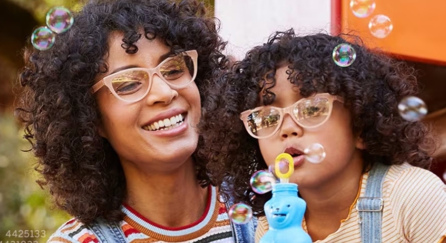 Woman and child wearing glasses blowing bubbles with a blue bubble toy.