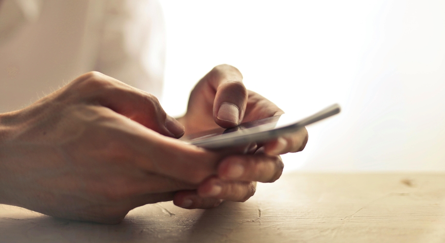 Hands holding a smartphone above a wooden surface.