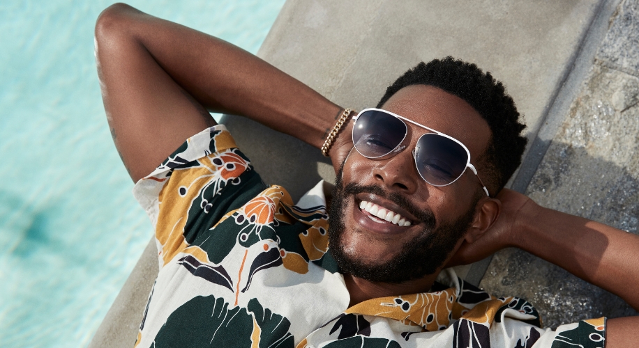 Man wearing sunglasses and a patterned shirt, smiling and lying down with hands behind his head.