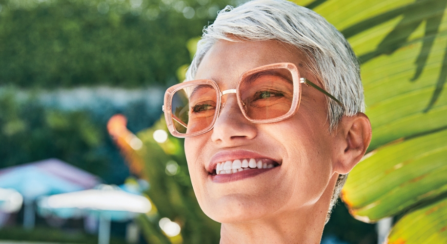 Person wearing square, pink-tinted glasses with a broad smile.