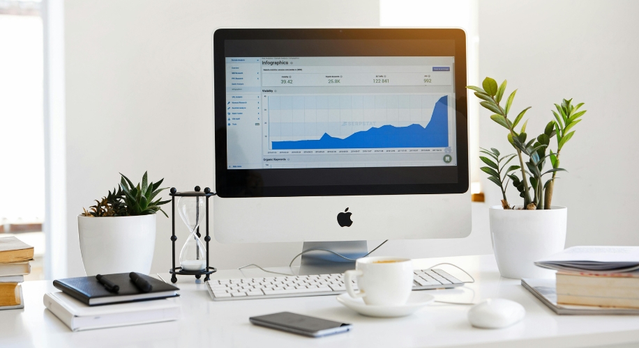 Apple iMac displaying a graph of website analytics, with a keyboard, mouse, and coffee cup on the desk.