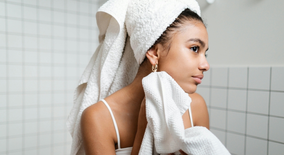 Woman drying face with a white towel, hair wrapped in another towel.