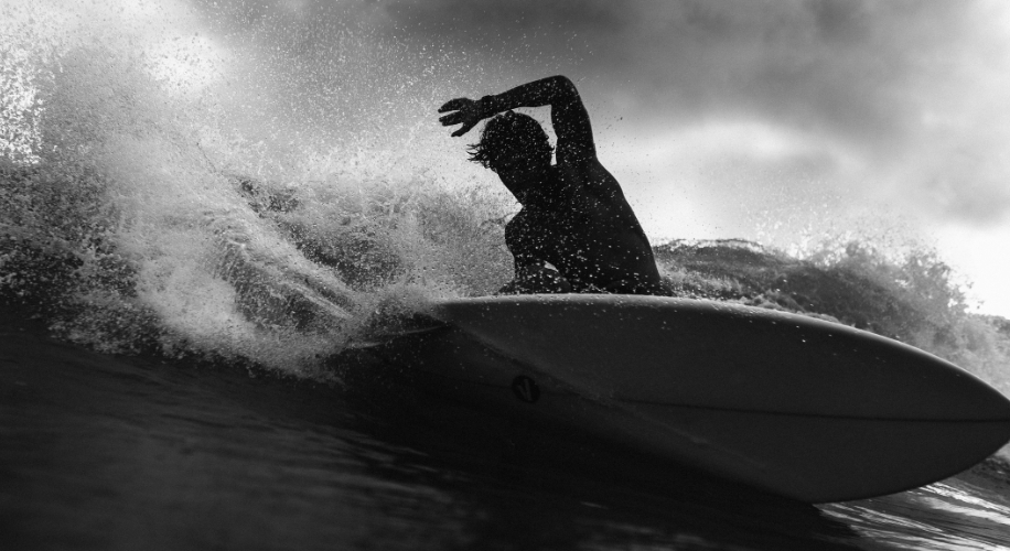 Surfer riding a wave on a surfboard in dynamic black and white.