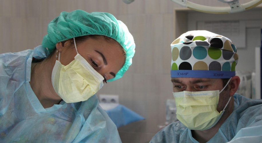 Two surgeons wearing masks and scrubs, focused on a medical procedure.