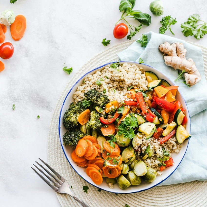 Bowl of quinoa with cooked vegetables including broccoli, carrots, brussels sprouts, zucchini, and red bell peppers.