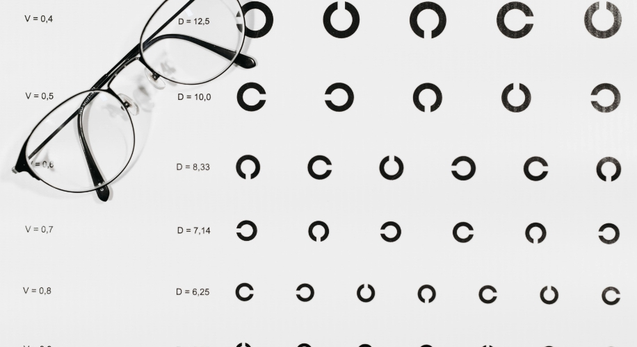 Black eyeglasses on an eye chart with rotating C-shaped symbols and readings V = 0.4, D = 12.5; V = 0.5, D = 10.0; V = 0.6,