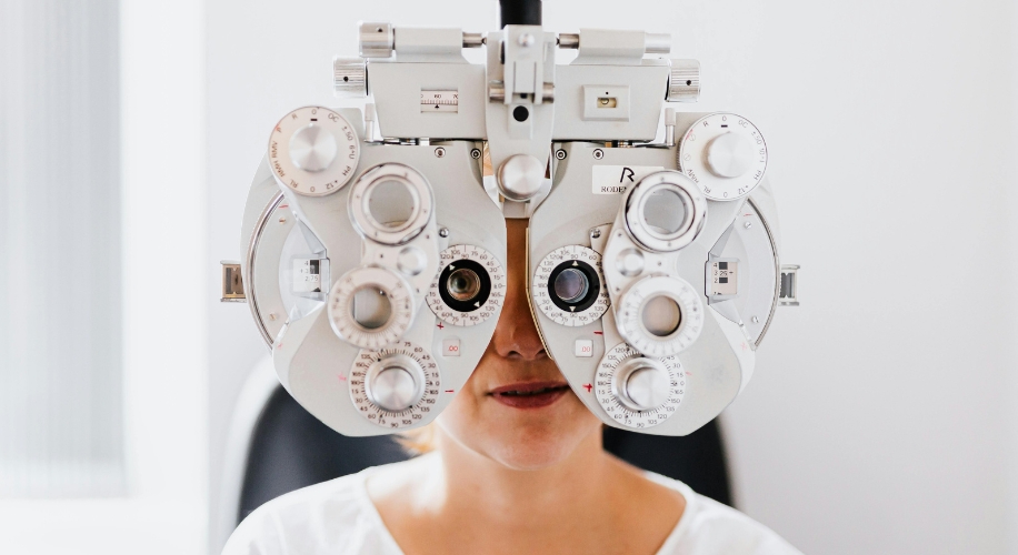 Phoropter used for eye exams, over a person&#039;s face. It has multiple dials and lenses for vision testing.