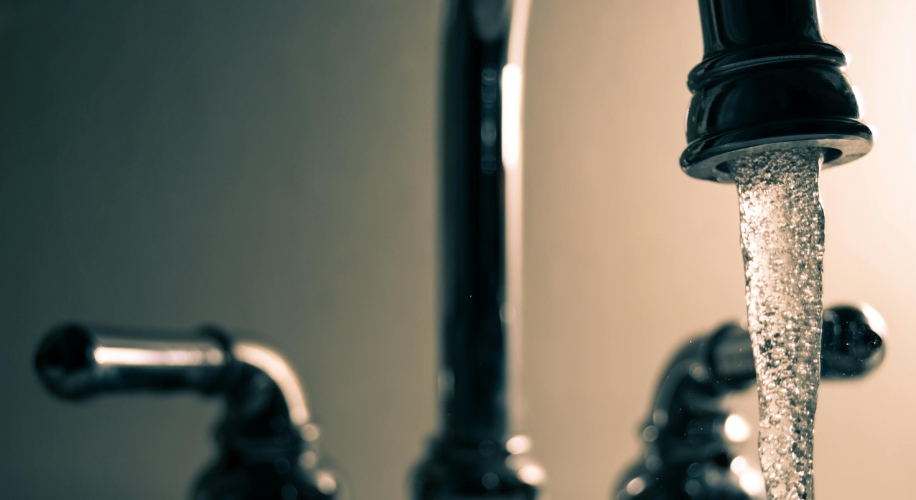 Water flowing from a chrome faucet. Two faucet handles visible in the background.