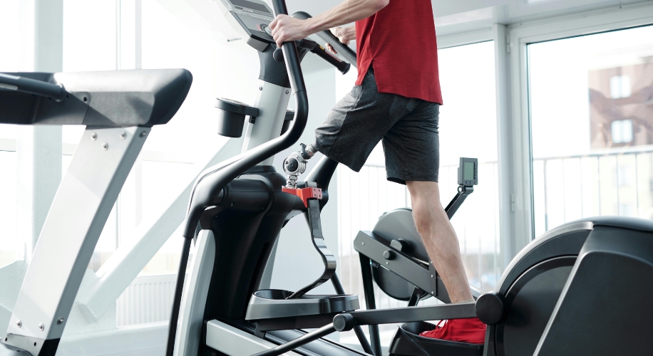 Person exercising on an elliptical machine in a bright, modern indoor gym setting.