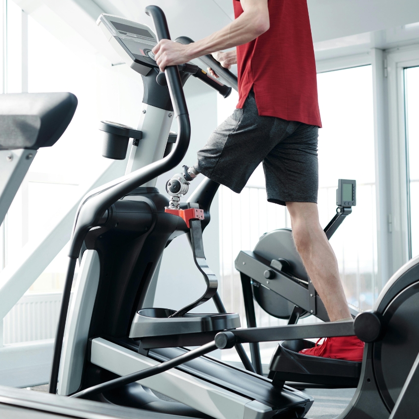 Person wearing a red shirt using an elliptical machine in a gym.