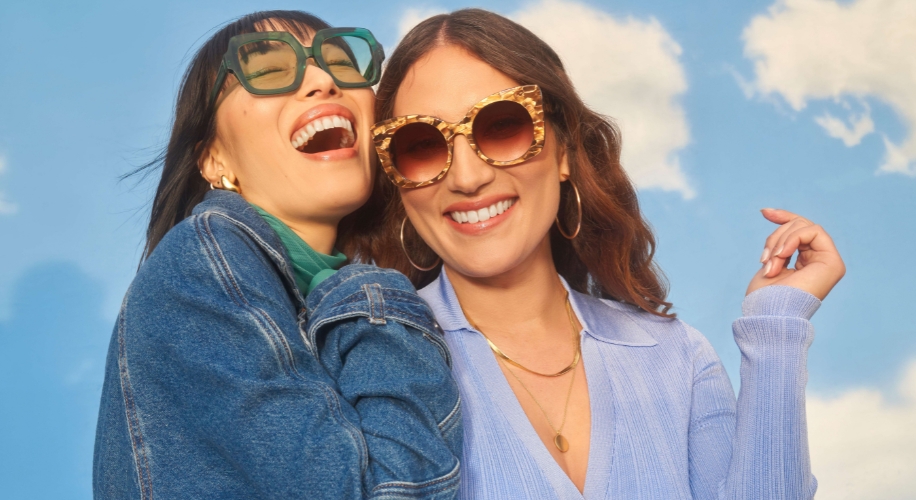 Women wearing stylish sunglasses, one in green frames, the other in tortoiseshell pattern frames.