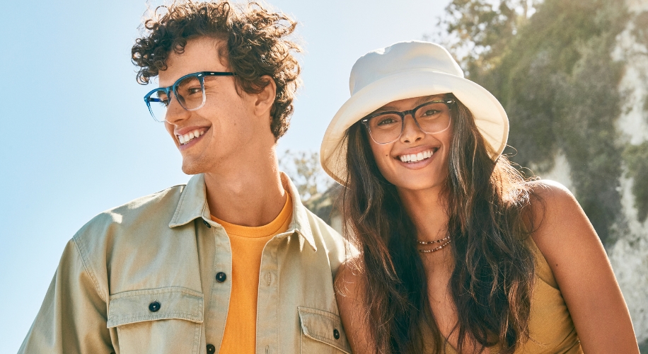 Two people wearing stylish eyeglasses, one in blue frames and the other in brown frames with a white hat.