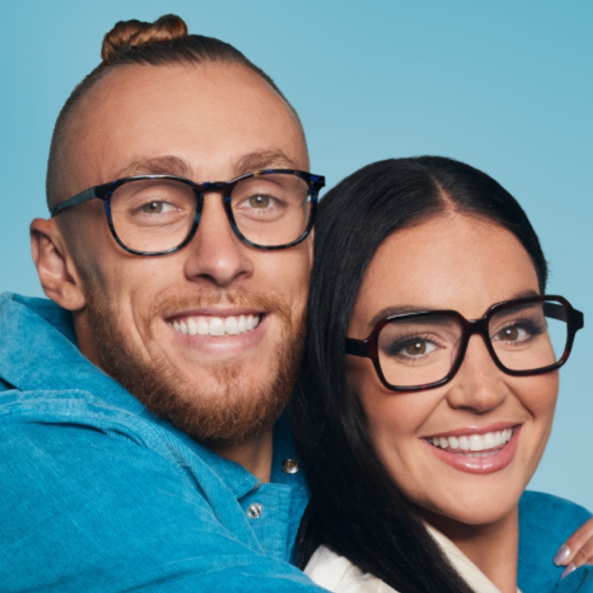 Two people wearing stylish, bold-framed glasses, smiling against a blue background.