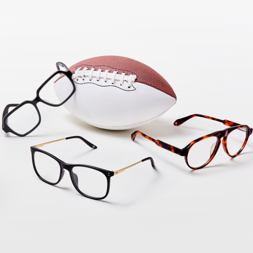 Three pairs of glasses, black square, black with gold arms, tortoiseshell round, near a football.