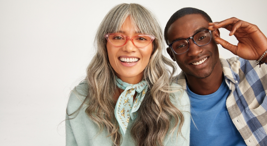 Two people wearing stylish eyeglasses, one in pink frames, the other in black frames, smiling.