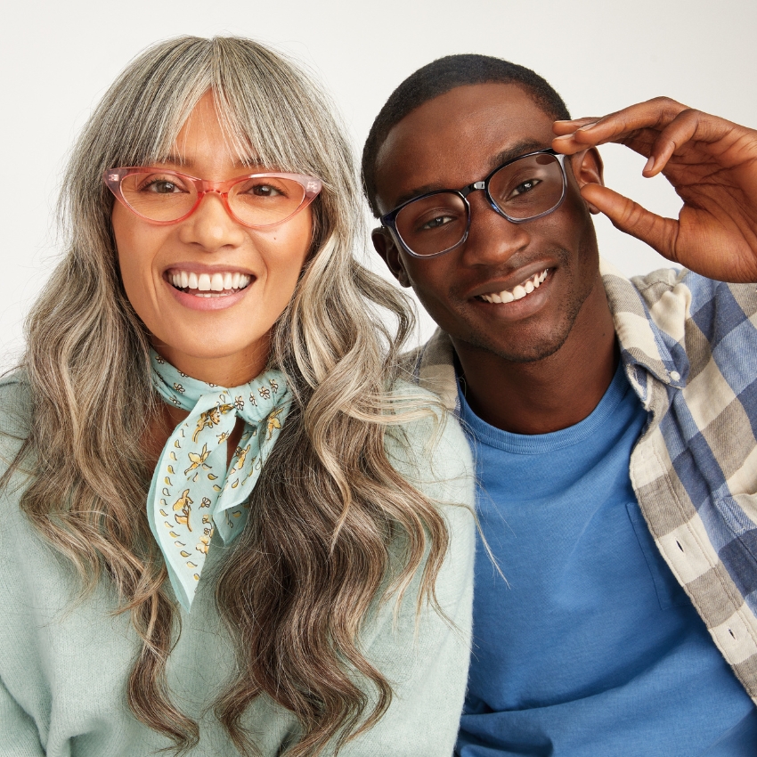 Two people wearing colorful eyeglasses, one in pink and the other in blue frames, smiling.