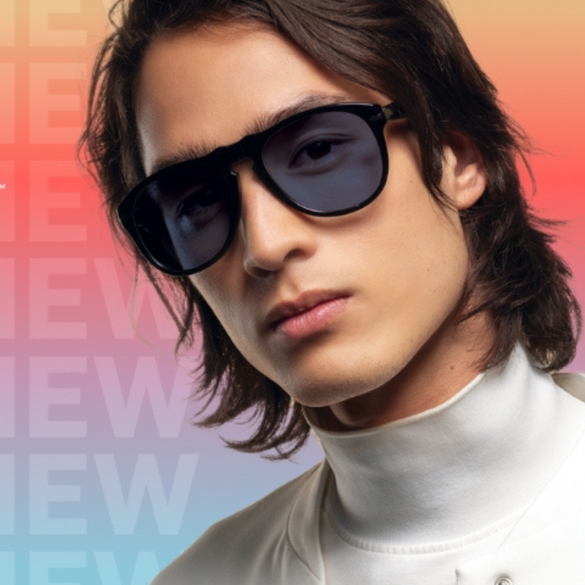 Sunglasses with dark lenses and black frames worn by a model. Background text: "NEW NEW NEW".