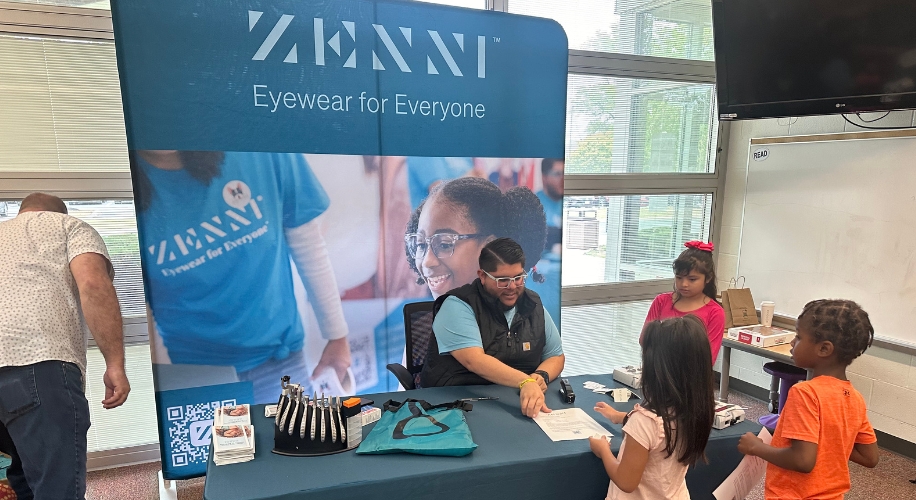 Zenni booth with &quot;Eyewear for Everyone&quot; banner, glasses display, and children at the table.