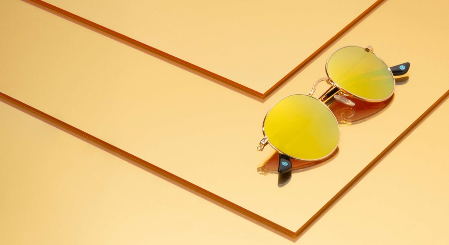 Yellow-lensed sunglasses with gold frames on a layered golden background.