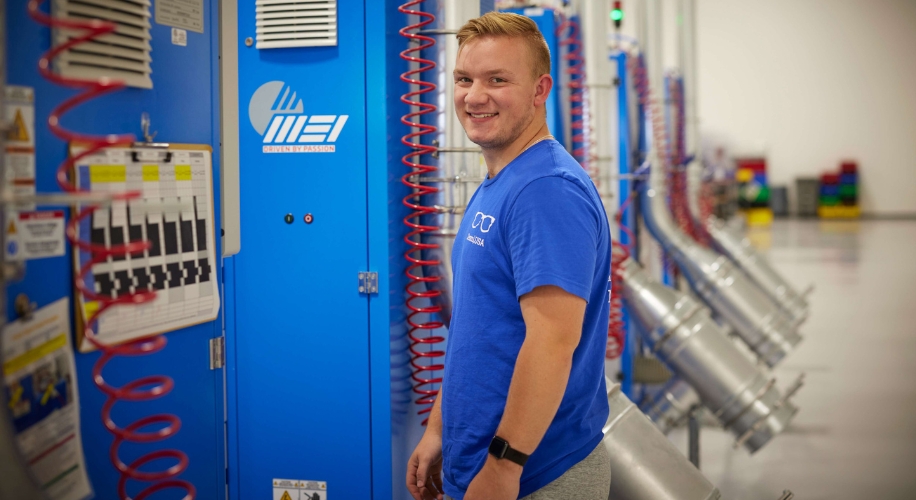 Man standing by blue MEI industrial machine with a control panel and red coils.