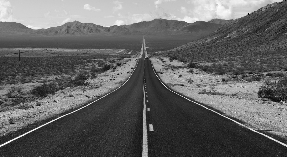 Desert highway stretching into distant mountains under a cloudy sky.