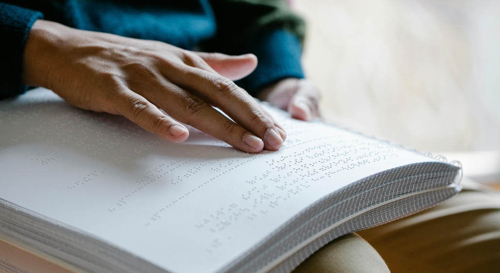 Hand reading a Braille book with spiral binding.