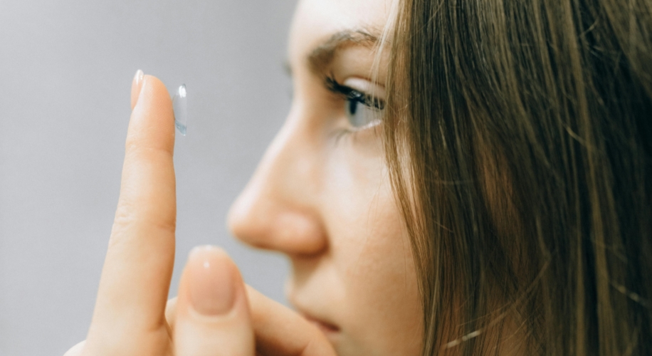 Close-up of a person holding a contact lens on their finger near their eye.