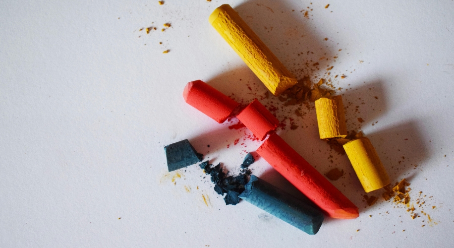 Red, yellow, and blue pastel chalk sticks with scattered chalk dust on a white surface.