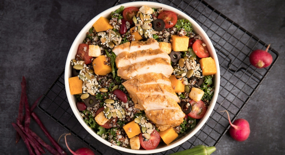 Grilled chicken salad with quinoa, pumpkin seeds, cheese cubes, cherry tomatoes, and greens.