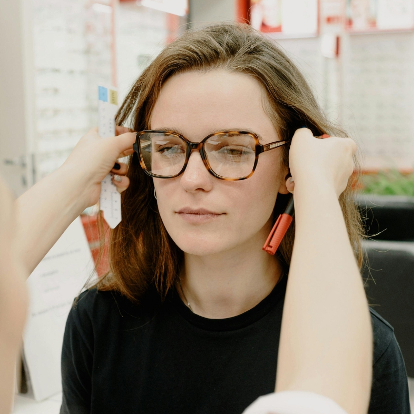 Woman wearing tortoiseshell glasses being fitted with a red-tipped measuring tool.