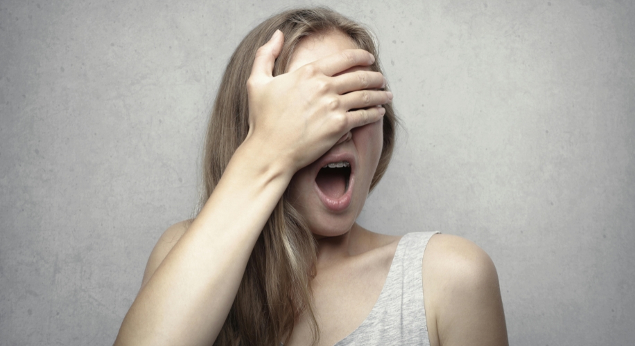 Woman covering one eye with hand, mouth open in surprise.