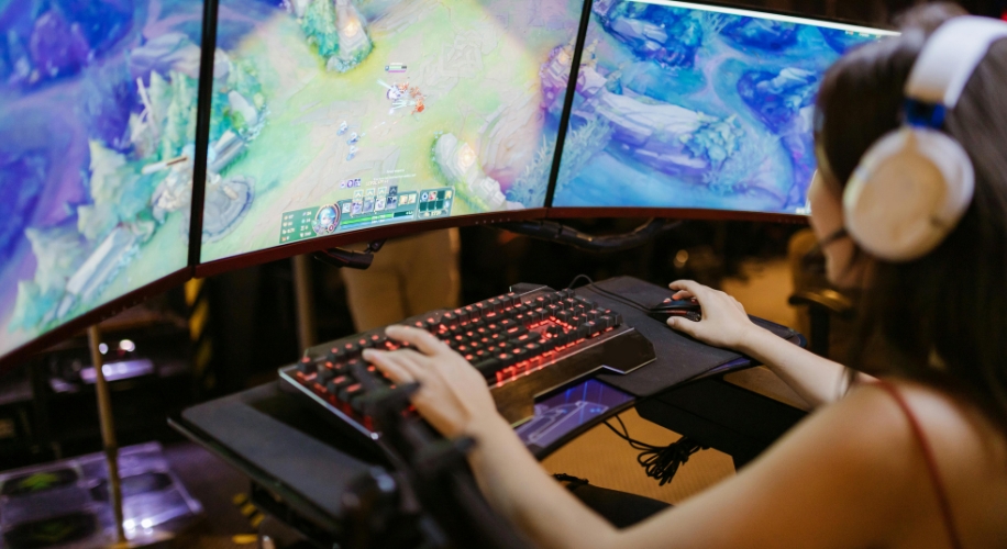 Curved triple-monitor gaming setup with red backlit keyboard and person wearing white headphones.