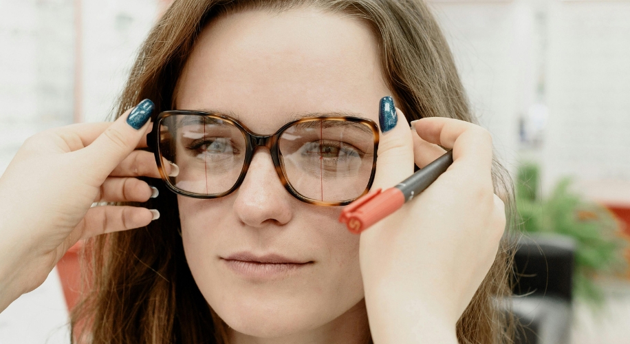 Woman trying on tortoiseshell glasses. A pen marks lens alignment.