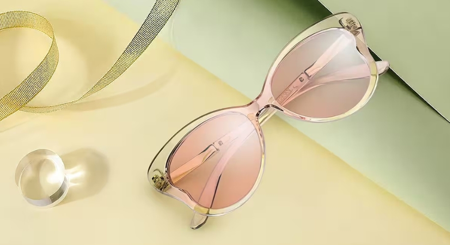 Cat-eye sunglasses with pink lenses and clear frames on a yellow surface.