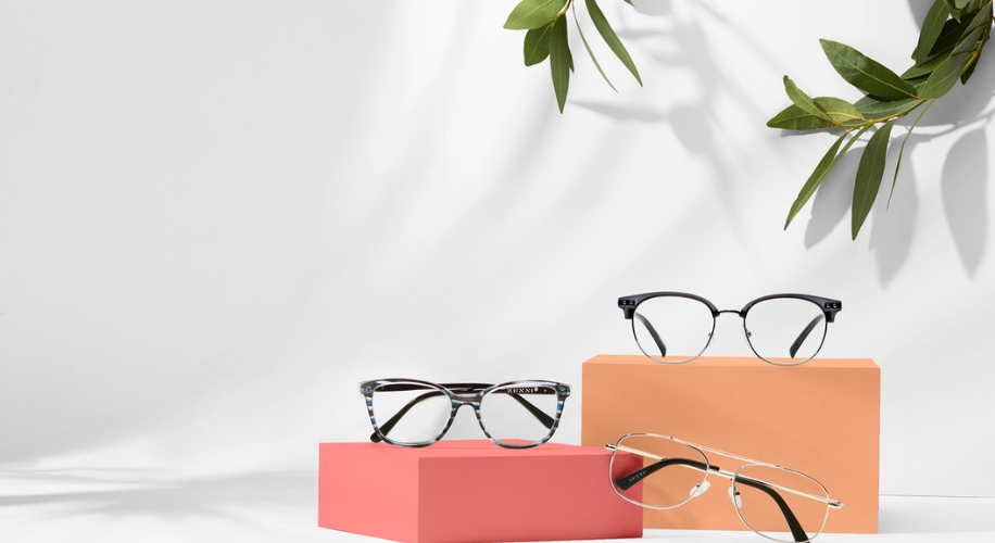 Three pairs of eyeglasses displayed on coral and peach blocks against a light background.