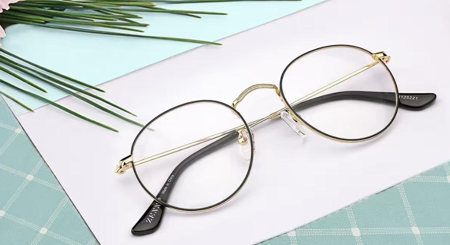 Gold-rimmed round eyeglasses on a white surface. Text on the temple: ZHAN YI 1725221.