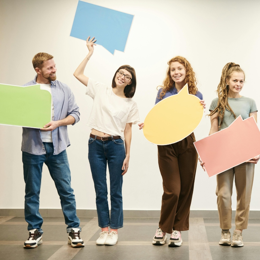 People holding colorful speech bubble cutouts: green, blue, yellow, and pink.