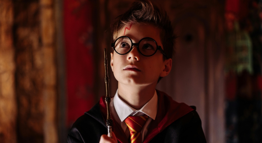 Child in wizard costume with round glasses and a wand.