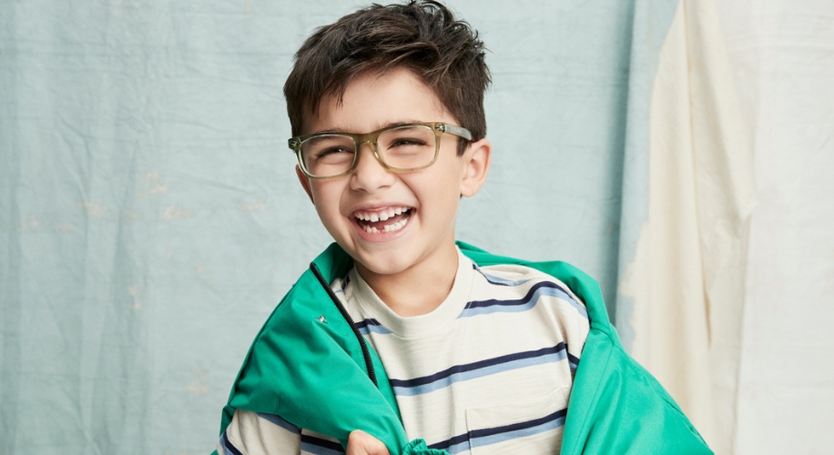 Child wearing green-framed glasses, smiling, in a striped shirt and green jacket.