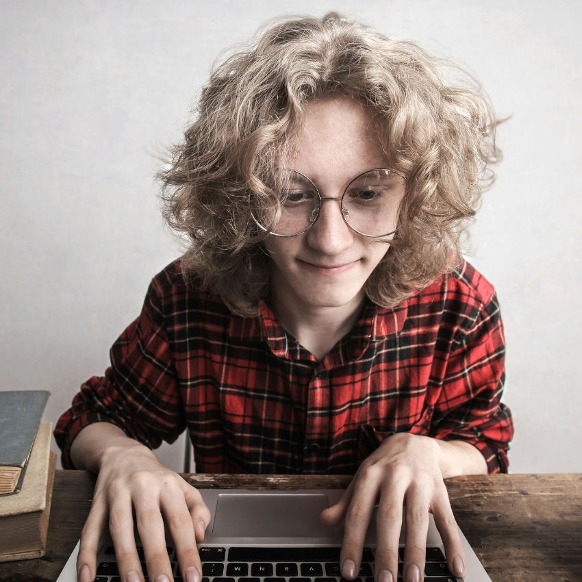 Person typing on a laptop, wearing glasses and a red plaid shirt.