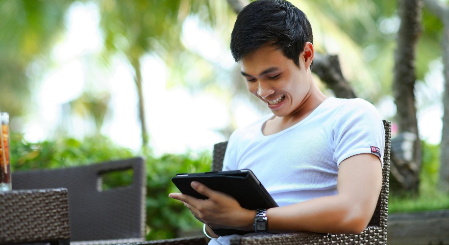 Person smiling while using a tablet outdoors.